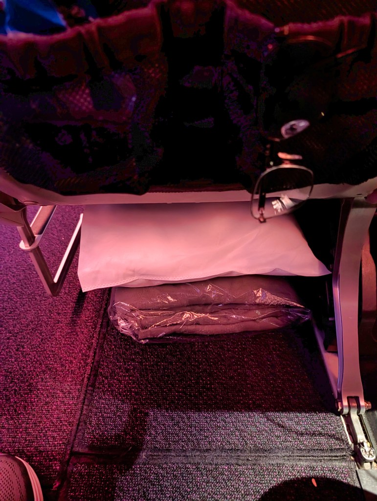 Pillow and blanket placed under seat in footwell area of Qatar Airways economy class